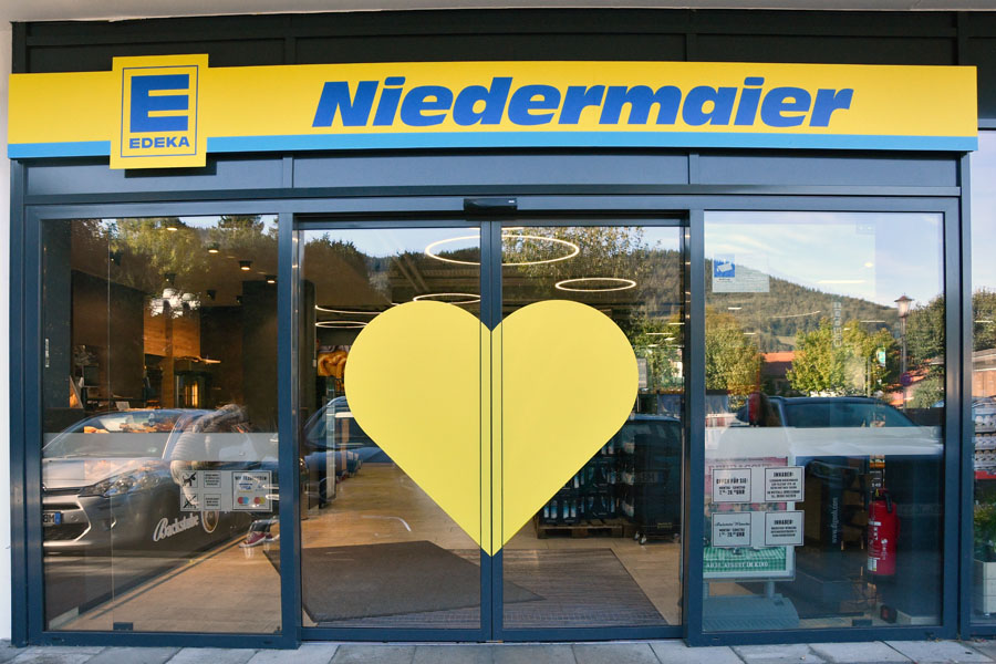 Eingang von EDEKA Niedermaier mit gelbem Herz auf der Glastür.